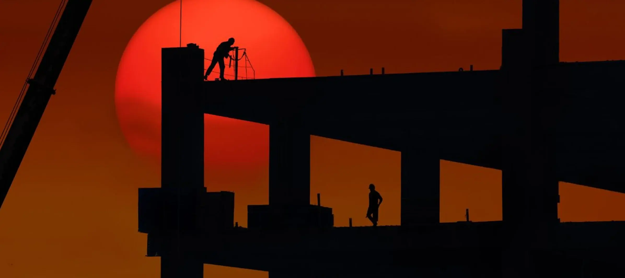 Construction workers silhouetted against a red sun on a building frame