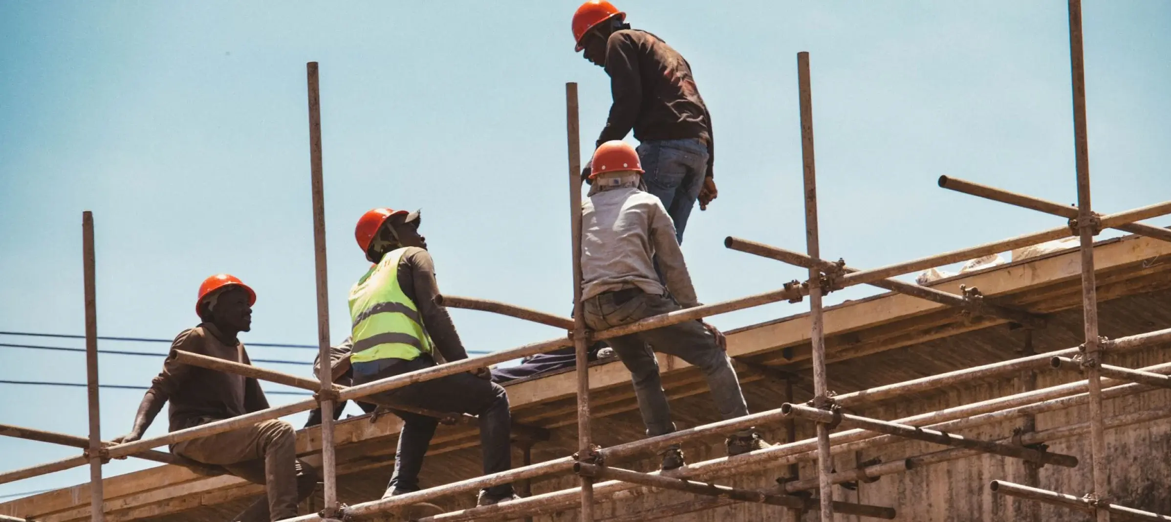 Nigerian construction crew in hard hats working on scaffolding against a blue sky