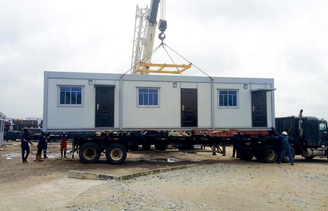Crane lifting a modular accommodation unit onto a flatbed trailer as the crew guides it