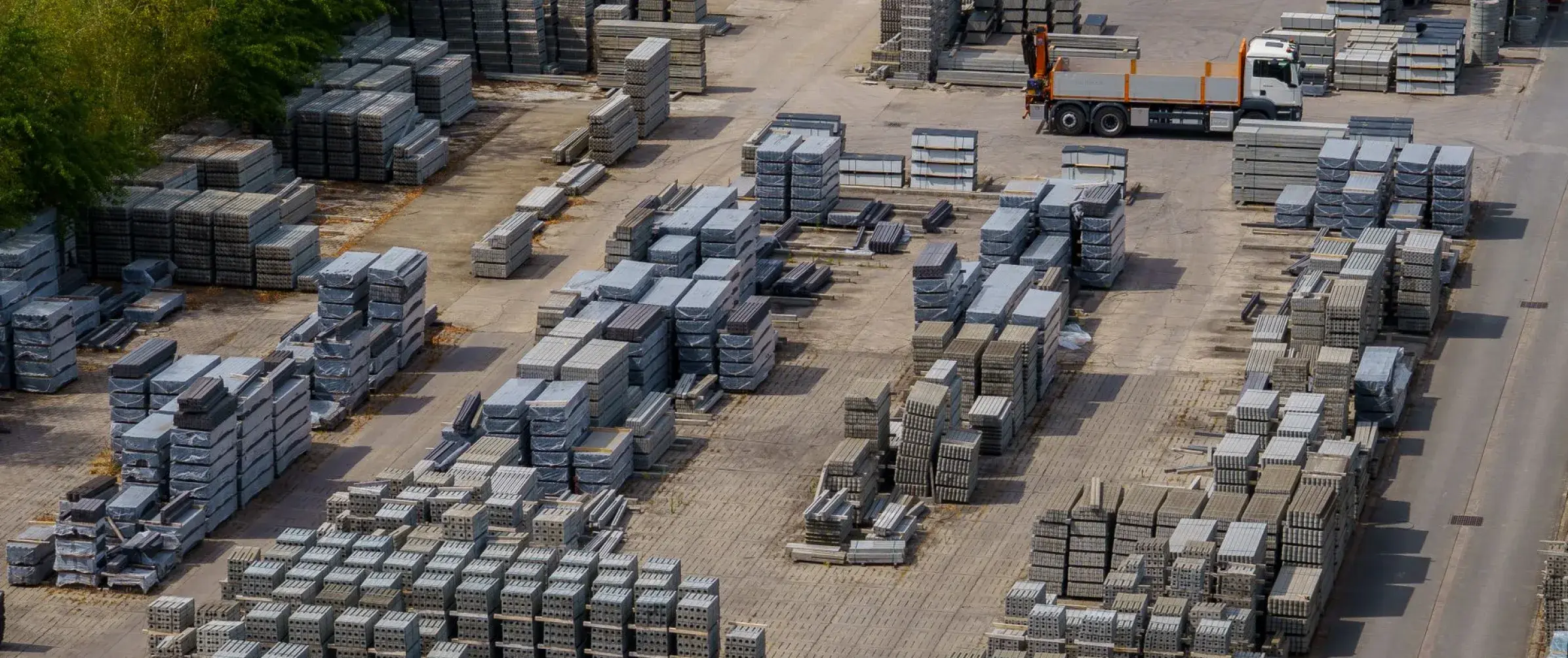 Aerial view of a materials yard stacked with pallets of precast concrete, with a flatbed crane truck loading