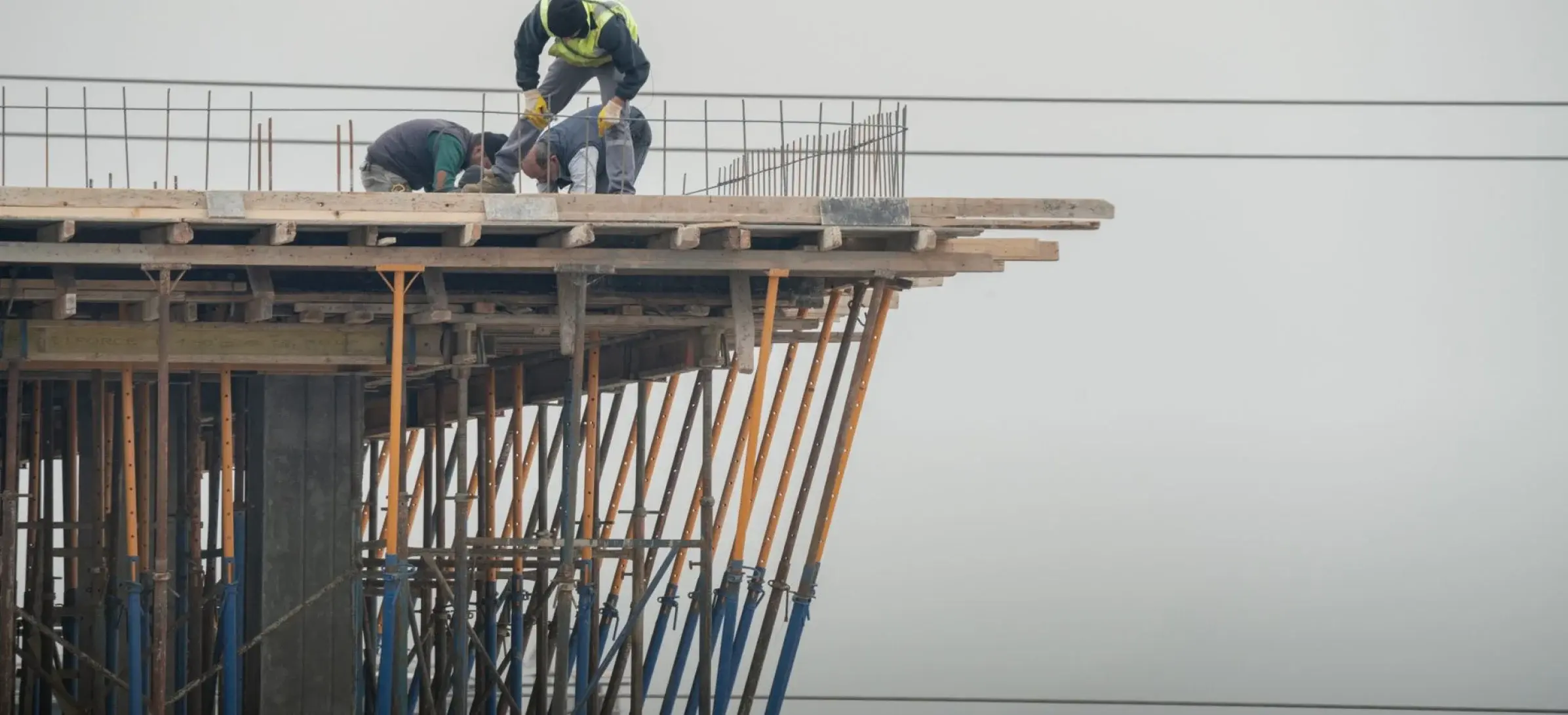 Construction crew tying rebar on a formwork deck supported by steel props