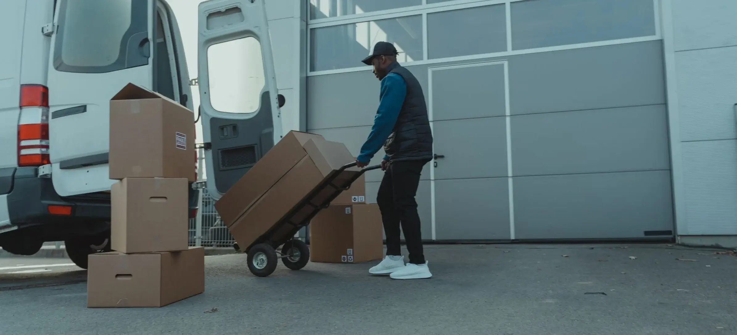 Logistics worker wheeling boxed supplies on a hand truck from a delivery van