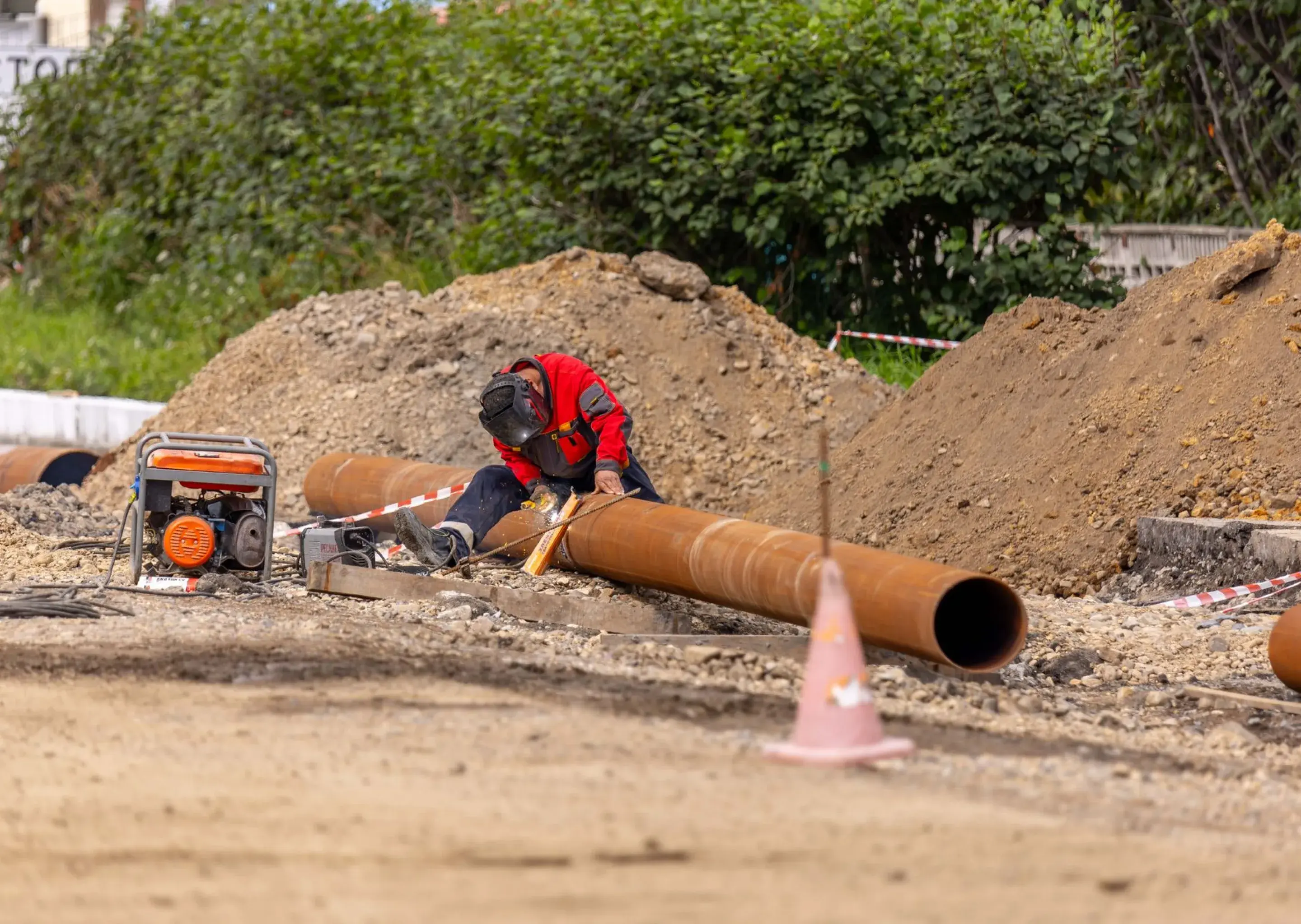 Welder in a protective mask joining a steel pipeline section on an excavation site